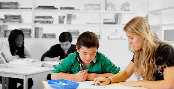 Kinder sitzen an Tischen und machen Schulaufgaben